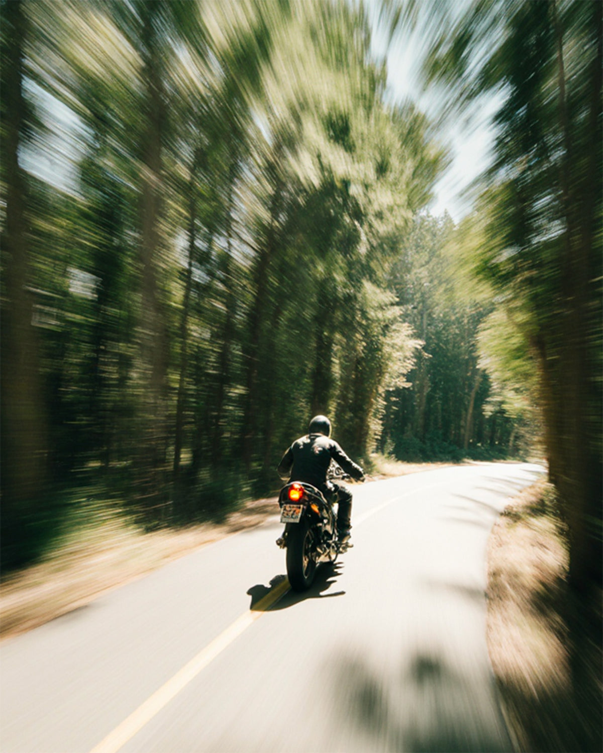 Le lenti sfumate sono adatte ad ogni condizione di luce. Nella foto una strada con sole e ombra e un motociclista che guida sicuro, grazie agli occhiali con lenti sfumate.