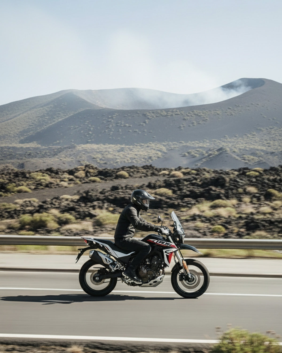 Foto che rappresenta un motociclista che pratica mototurismo vicino ad una zona montuosa con vulcani. 